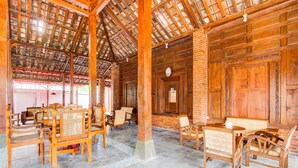 A spacious room with wooden furniture, a high ceiling with exposed beams, and a brick wall. - Capital O 93873 Sokkyo Homestay (Ngaglik)