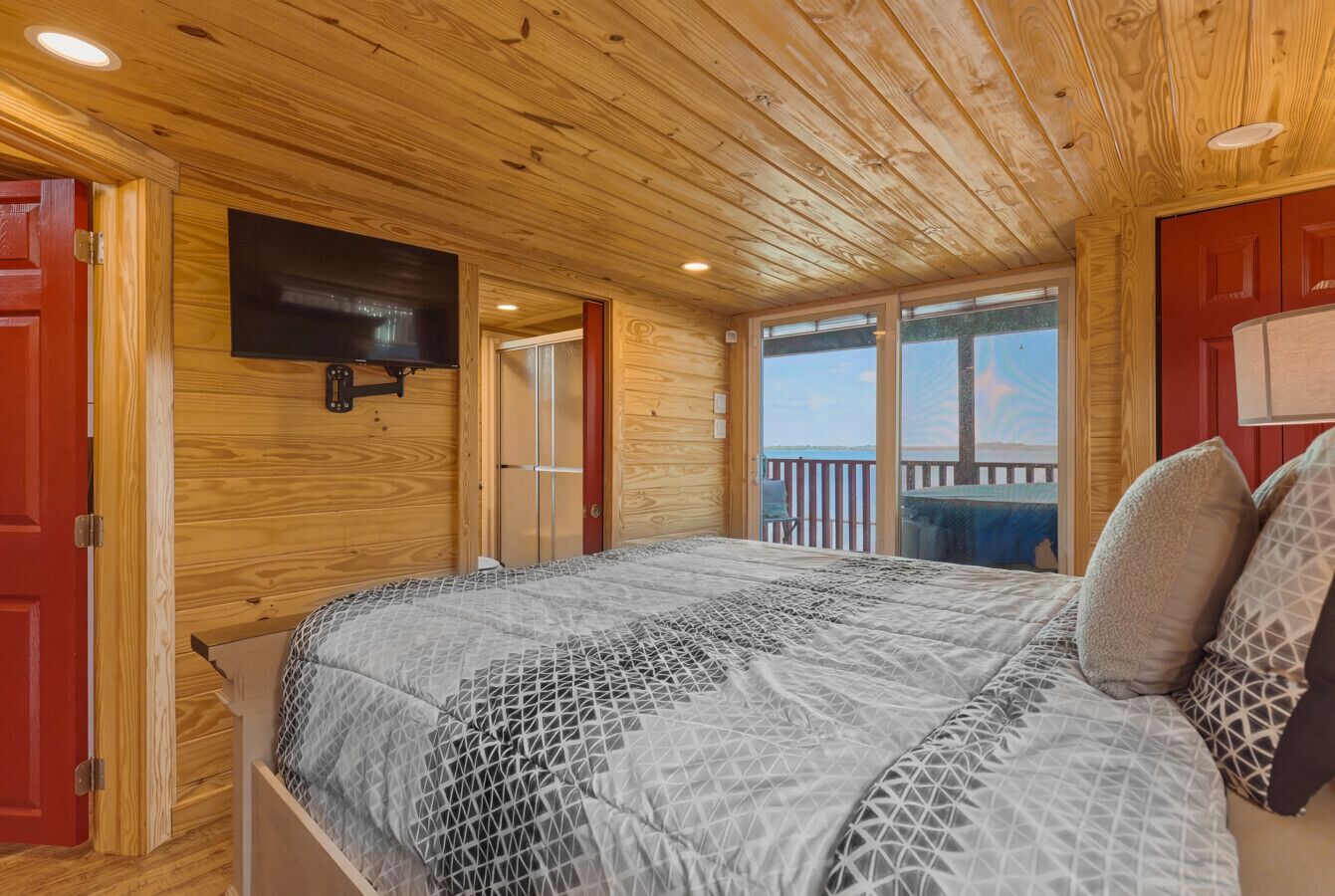 A wooden-paneled bedroom with a bed, a mounted TV, and a balcony with a view.