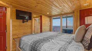 A wooden-paneled bedroom with a bed, a mounted TV, and a balcony with a view.