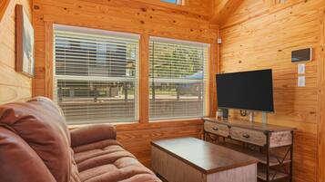 Ein Holzblock-Interieur mit einer Couch, einem Fernseher auf einem Schrank und großen Fenstern mit Jalousien.