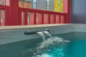 A hot tub with a water spout, surrounded by a red wooden deck.
