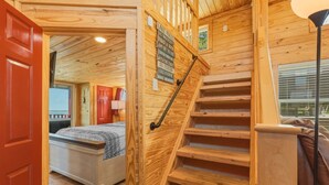 A wooden staircase with a handrail, a bed in the adjacent room, and a red door. - Lake Front Cottage Paradise! (Pittsburg)