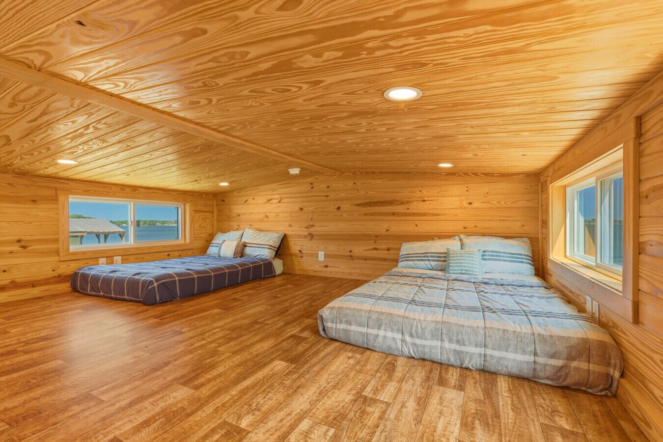 A cabin with two beds, wooden floors, and a large window.