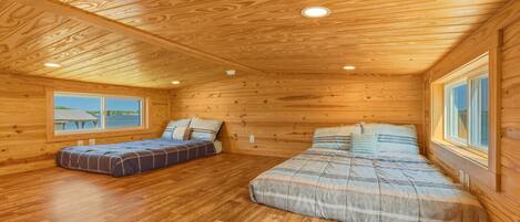 A cabin with two beds, wooden floors, and a large window.