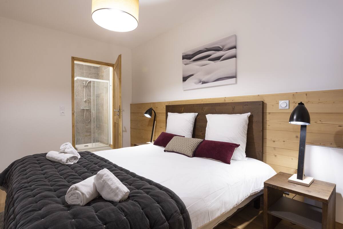 Ein Schlafzimmer mit einem großen Bett, einem Holzkopfende, einer Nachttischlampe und einem Duschbereich.