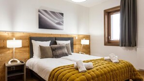 Una camera d'hotel con una testiera in legno, un letto grande con copripiumino color senape, due lampade sui comodini, un'opera d'arte incorniciata sopra il letto e una finestra con tende.