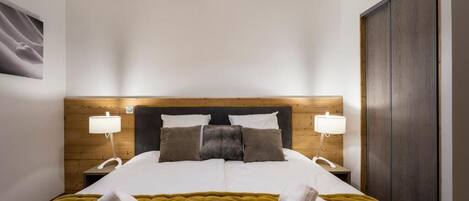 A neatly made bed with a tufted headboard, two bedside lamps, and a pair of rolled towels on the bed.