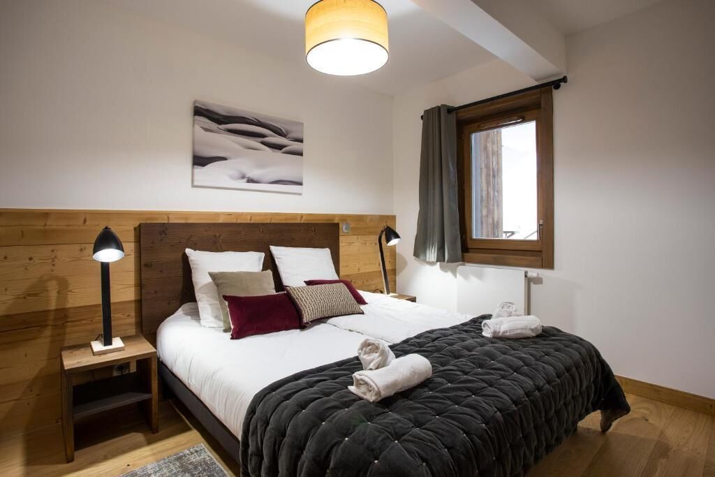 Een slaapkamer met een houten hoofdbord, een groot bed met witte lakens, twee bedlampjes, een raam met gordijnen en een schilderij aan de muur.
