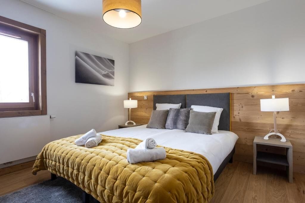 A hotel room with a large bed, two bedside lamps, a wooden headboard, a window, and a painting on the wall.