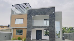 A modern two-story house with a flat roof, large windows, and a balcony.