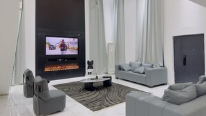 A modern living room with a flat-screen TV, grey sofas, a fireplace, and a large window with curtains.