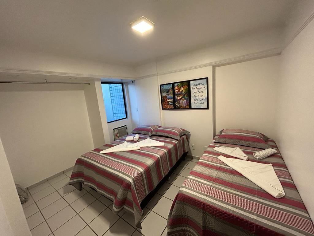 A room with two beds, each with striped bedding and pillows. There is a framed artwork on the wall and a window with blinds.
