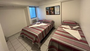 Une chambre avec deux lits, chacun agrémenté de draps et d’oreillers à rayures. Un tableau encadré orne le mur, et une fenêtre est équipée de stores.