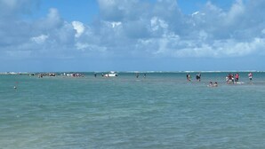 Une plage avec une eau d’un bleu limpide et quelques personnes visibles au loin.