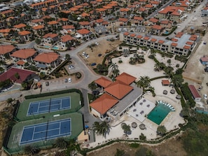 An aerial view of a residential area with multiple buildings, a tennis court, and a swimming pool.