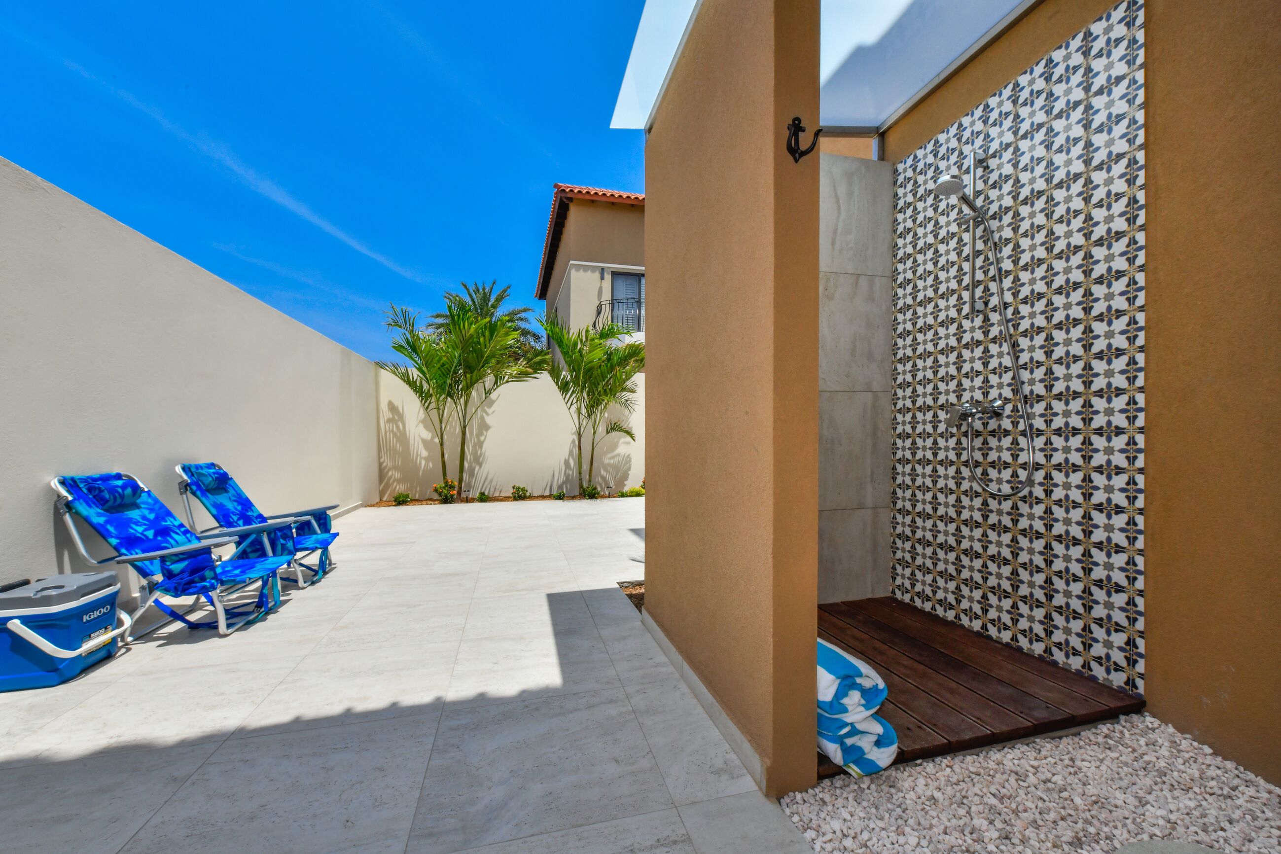 A sunlit outdoor area with a pool, lounge chairs, and a tiled shower area.