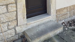 Eine Fassade aus Stein mit einer dunkelbraunen Tür, einem kleinen Betonschritt und einer Wandleuchte.