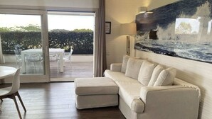 A modern living room with a beige sectional sofa, a dining table with chairs, and a large window overlooking a garden. - LIKE at HOME ​PALAU n° 11 Poolside Paradise Patio (Palau)
