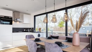 Une cuisine moderne avec des meubles blancs, une table à manger en bois et des luminaires suspendus.