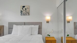Une chambre à coucher bien rangée, avec un lit, des tables de chevet, une lampe fixée au mur et un miroir.