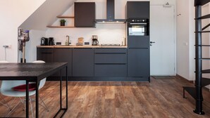 Una cocina moderna con muebles oscuros, horno empotrado y comedor con mesa y sillas.