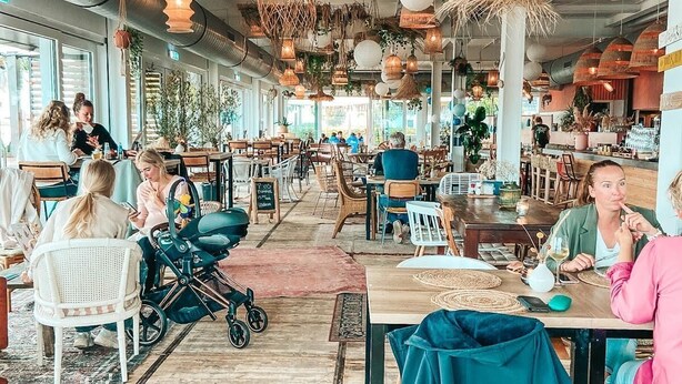 Un café espacioso con techos altos, lámparas de mimbre colgantes y diversas opciones de asiento, incluyendo mesas y sillas.