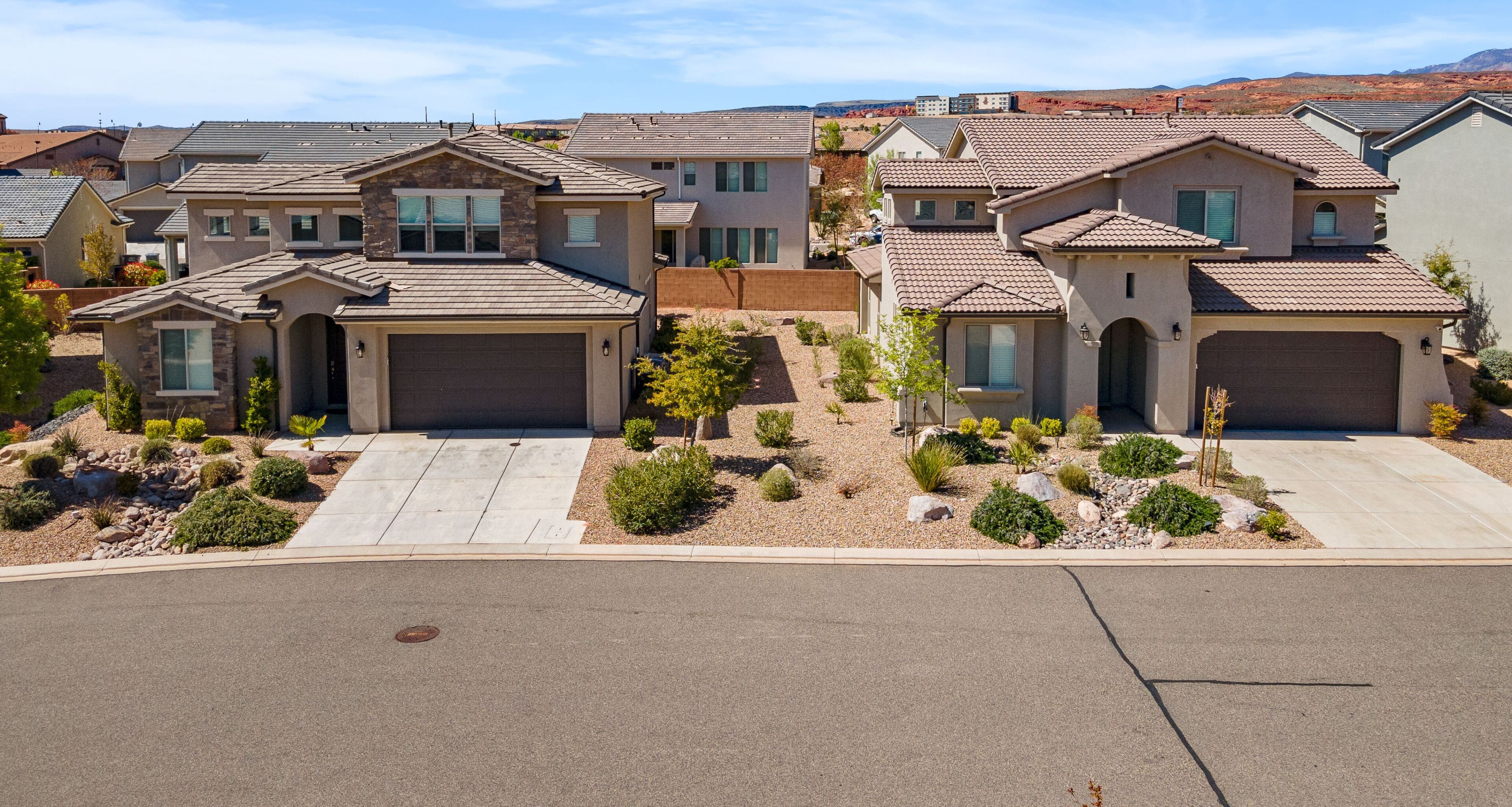 A residential area with multiple two-story houses featuring attached garages, landscaped front yards with small shrubs and trees, and a clear view of the surrounding landscape.