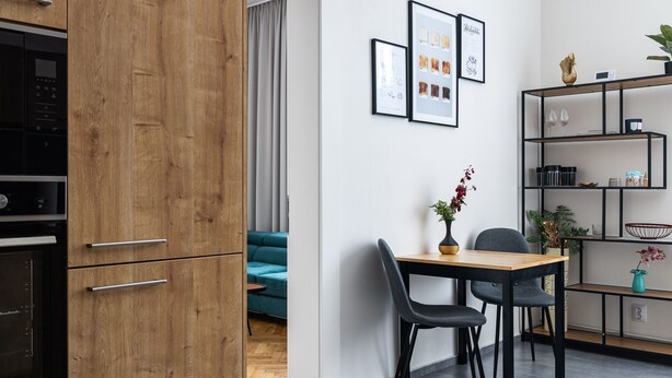A modern kitchen with wooden cabinets, a dining area with a table and chairs, and a living room with a sofa. - City Buzz Apartment - O2 Arena - Sleeps 6 (Prague)