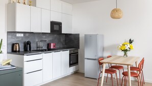 A modern kitchen with white cabinets, a black countertop, and a built-in oven. There is a dining table with red chairs and a vase of flowers.