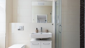 Een moderne badkamer met een wit toilet, een wastafel met zeepdispensers en een douchecabine van glas.