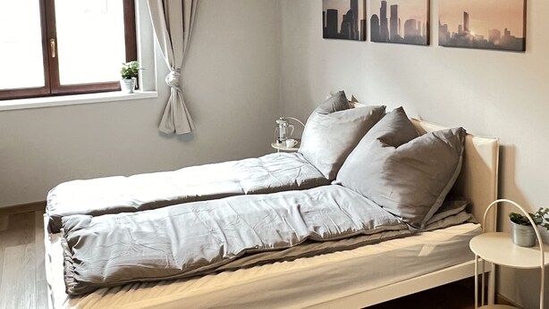 Ein modernes Schlafzimmer mit einem Bett, einem Nachttisch, einem Fenster mit Vorhängen und drei Stadtansichten an der Wand.