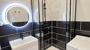 Une salle de bain moderne avec une douche à parois de verre, un lavabo blanc et un lave-linge compact.