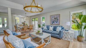 A spacious living room with a blue sofa, wooden armchairs, and a white coffee table. - Fire-Pit & Private Pool. On golf course. Palmetto Dunes, HHI.  (Hilton Head Island)
