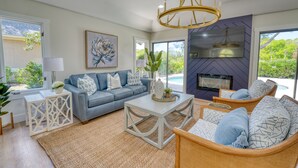 A modern living room with a sofa, coffee table, and chairs, a fireplace, and large windows with a view of greenery. - Fire-Pit & Private Pool. On golf course. Palmetto Dunes, HHI.  (Hilton Head Island)