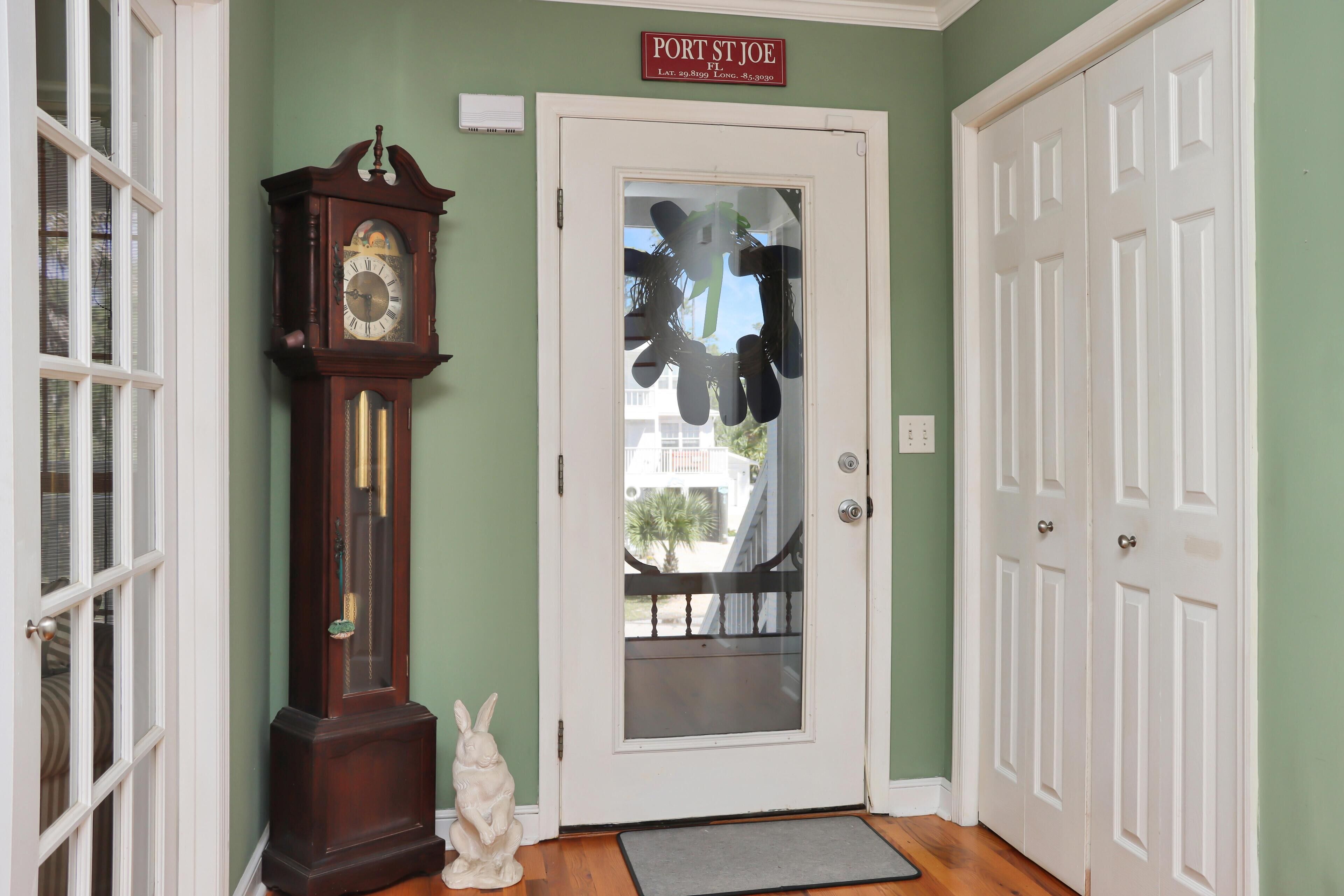 A hallway with a door labeled "Port St Joe FL," a wooden grandfather clock, a white rabbit statue, and a doormat.