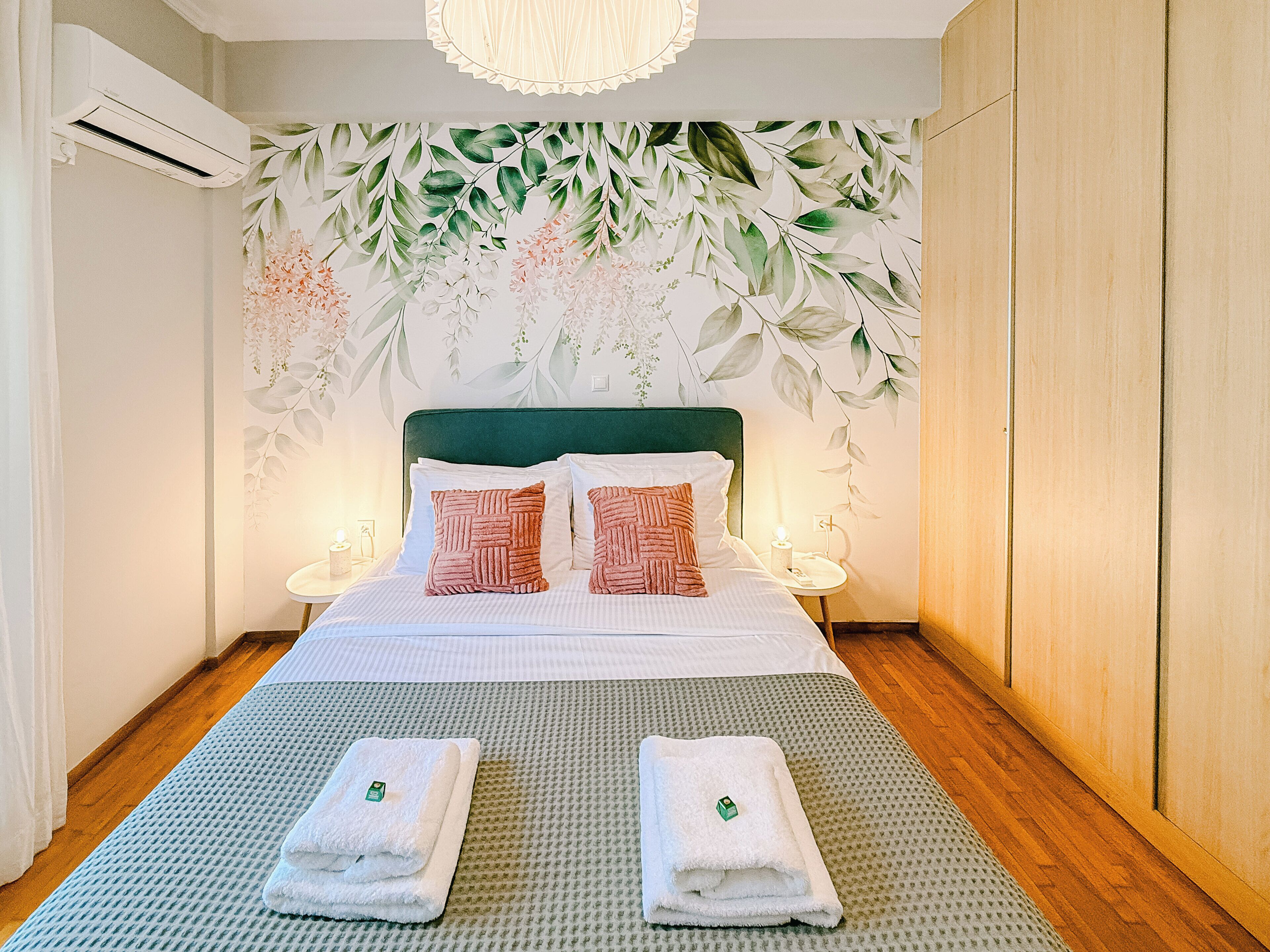 A neatly made bed with pillows, a green headboard, and a wall with a floral design.