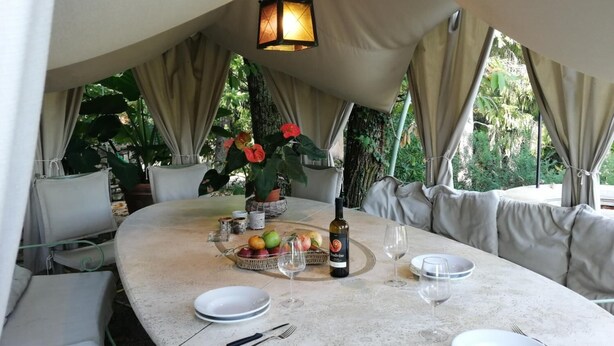 Una mesa de comedor redonda con una botella de vino, copas y una cesta de frutas.