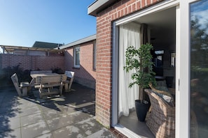 A patio with a table and chairs, a potted plant, and a sliding glass door leading to an interior space. - Familyhome - Oostkapelseweg 32 | Serooskerke 'Ooievaar' (Serooskerke)
