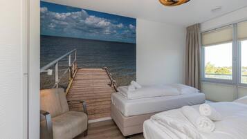 Een hotelkamer met een bed, een stoel, een houten terras dat naar een balkon leidt en uitzicht op zee.