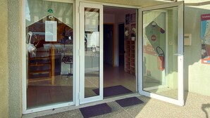 Entrada de un edificio con puertas de vidrio, suelo de baldosas y un pequeño espacio exterior con un felpudo.