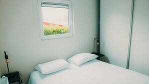 Una habitación luminosa y limpia, con una cama, una mesita de noche, una lámpara y una ventana con vistas al verdor.