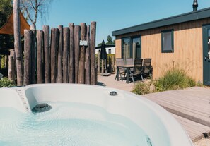 A wooden deck with a hot tub, a wooden fence, and a building with a modern design. - 4-persoons Voortse Villa Wellness (Voorthuizen)