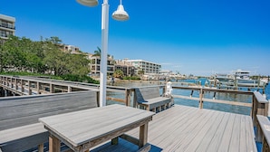 A wooden deck with benches and tables, overlooking a marina with boats and a clear blue sky. - Corner Intracoastal Condo heated pool/spa and steps to beach (Indian Shores)