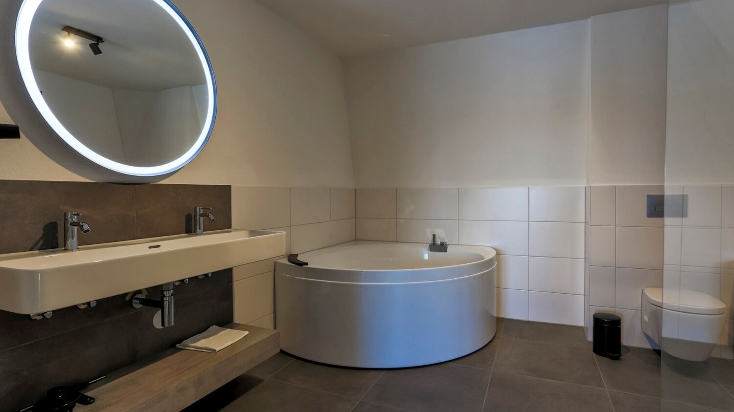 Een moderne badkamer met een rond bad, een rechthoekig wastafelmeubel en een grote spiegel.