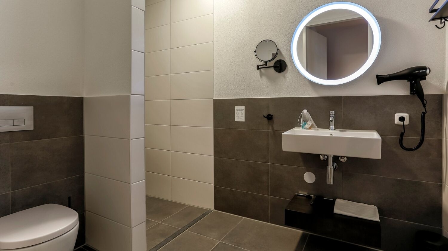 Une salle de bain comprenant des toilettes, un lavabo avec un miroir, un sèche-cheveux et un porte-serviettes.
