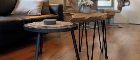 Una sala de estar moderna con un sofá de cuero negro, una mesa de centro redonda con posavasos tejido y una mesita de noche de madera con un jarrón de flores.