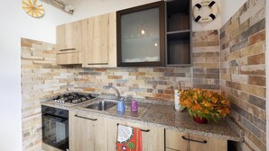 A kitchen with wooden cabinets, a gas stove, a sink, and a backsplash made of variously colored tiles. - Studio Timo - Studio Apartment, Sleeps 3 (Pompeiana)
