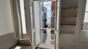 A room with a sofa, a small table, and a door leading to a balcony with a metal gate. - Porthos 111 - One Bedroom Apartment, Sleeps 4 (Roses)