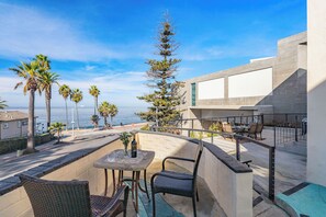 Un balcon avec une table et des chaises, donnant sur une zone côtière bordée de palmiers et offrant une vue sur la mer.