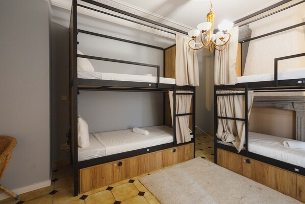 Une chambre avec des lits superposés, un lustre, des rideaux et un sol à motifs.